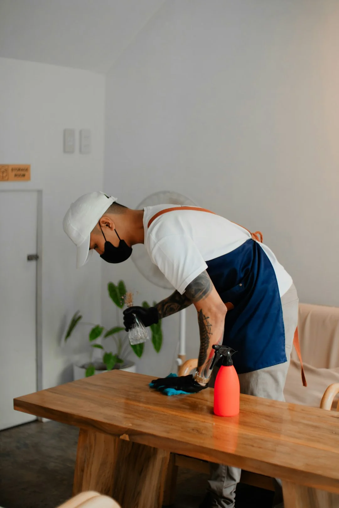 A detailed view of a hand cleaning a stovetop using a spray bottle and cloth.